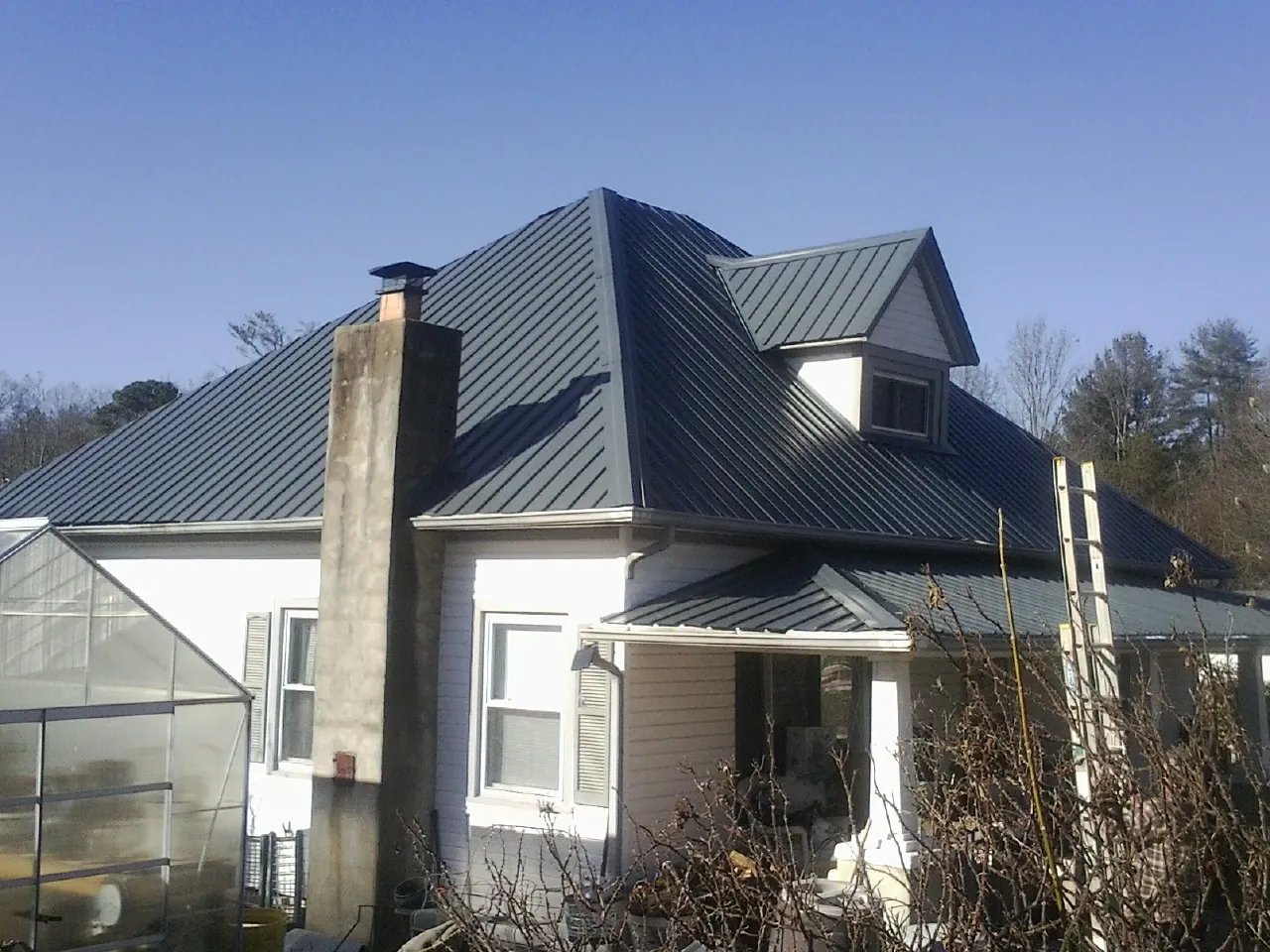Dark blue standing seam metal roof on a white farmhouse with dormer — Slate & Tile Roof Repair by Roofing Brothers in Sewell
