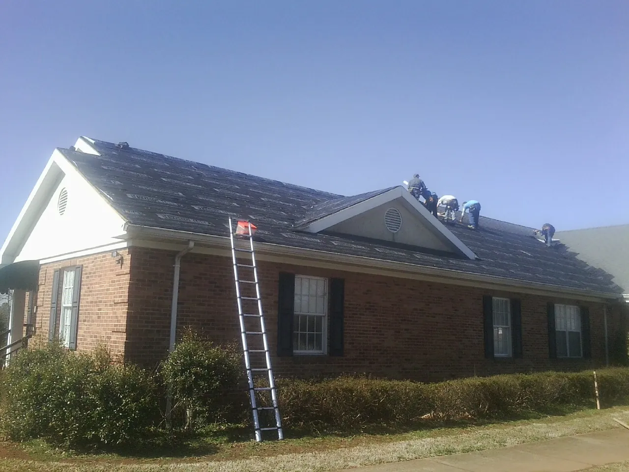Crew tearing shingles off a brick ranch roof with a ladder set — Metal Roof Repair work by our crew in Sewell