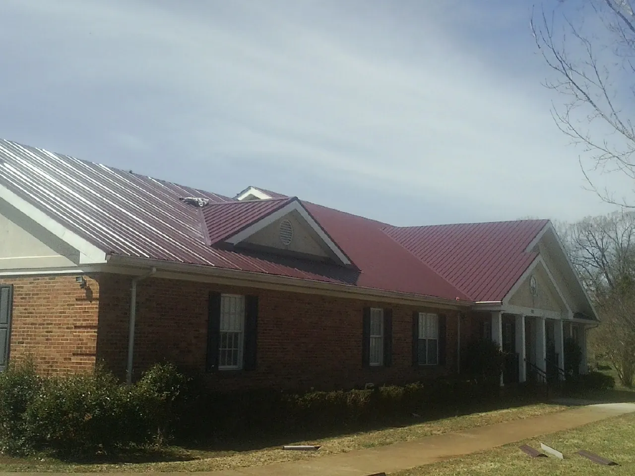 Red metal roof with gabled entries on a long brick building, from a Hail Damage Roof Repair job in Sewell