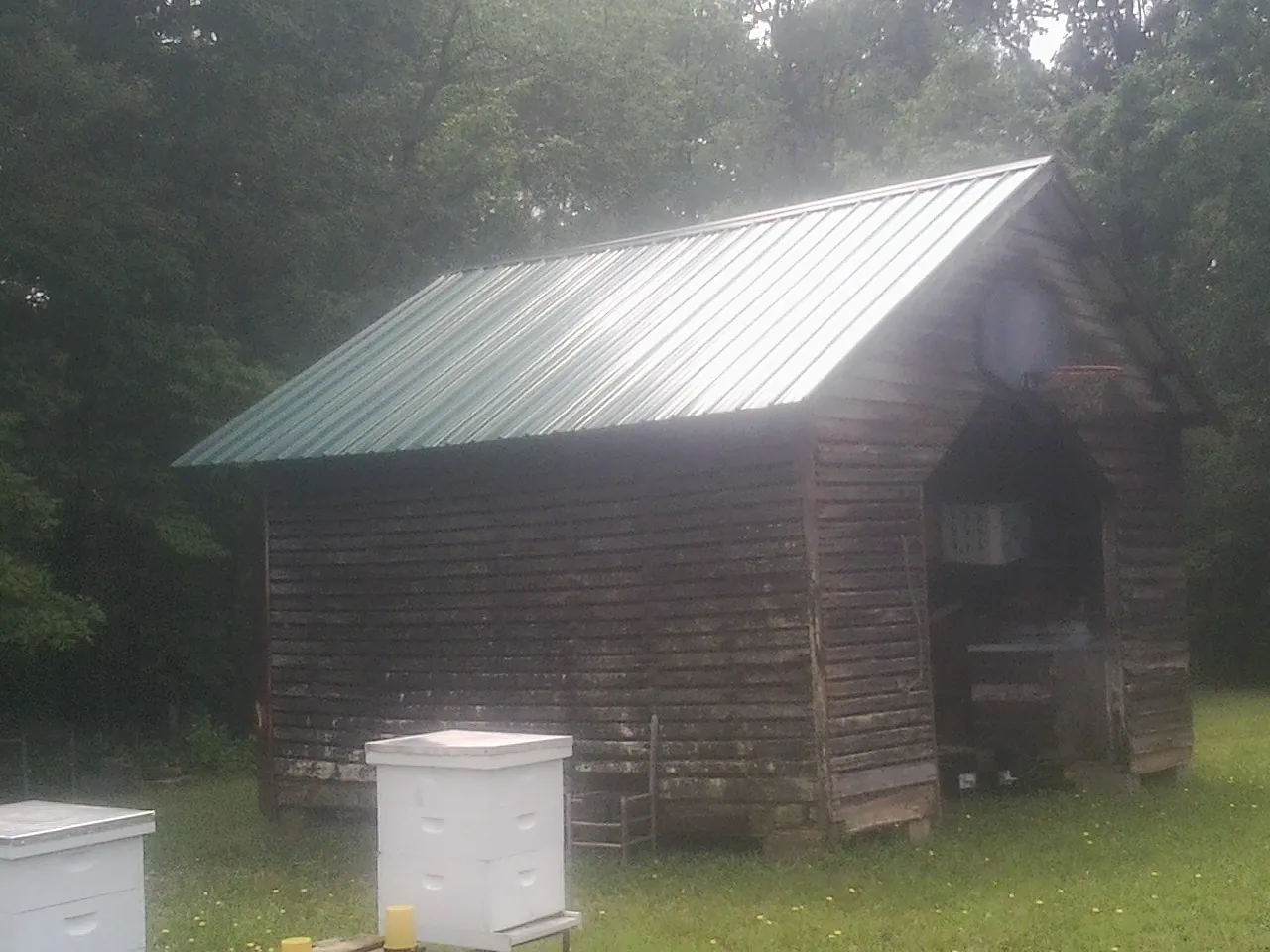 Green metal roof on a weathered barn beside stacked beehives in Sewell