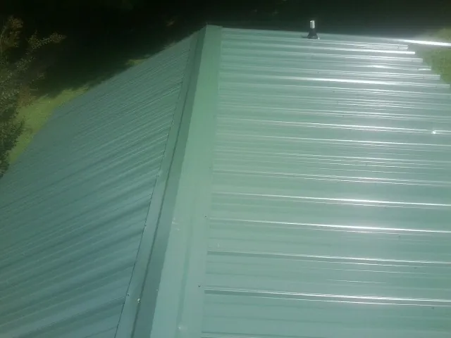 New green metal panels meeting at the ridge of a roof — Flat Roof Repair work by our crew in Sewell