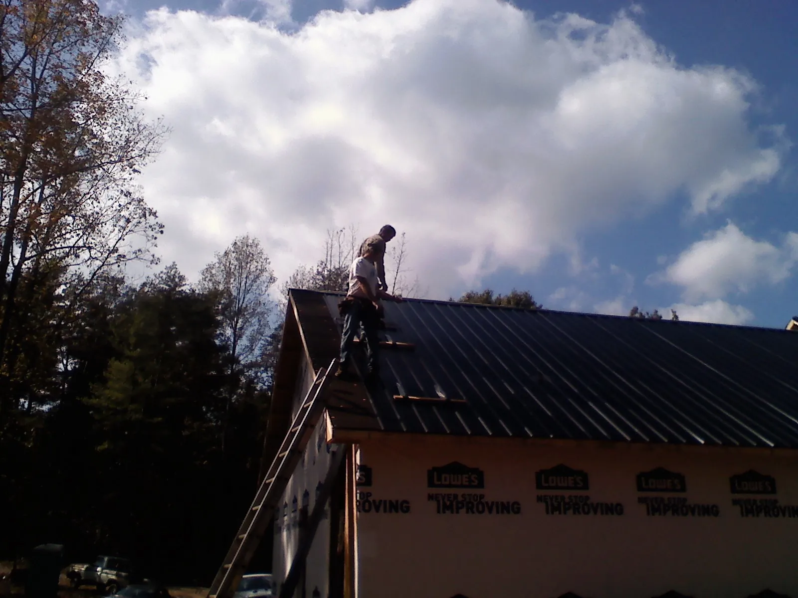 Roofer fastening dark metal panels high against a cloudy sky, from a Roof Inspection job in Sewell