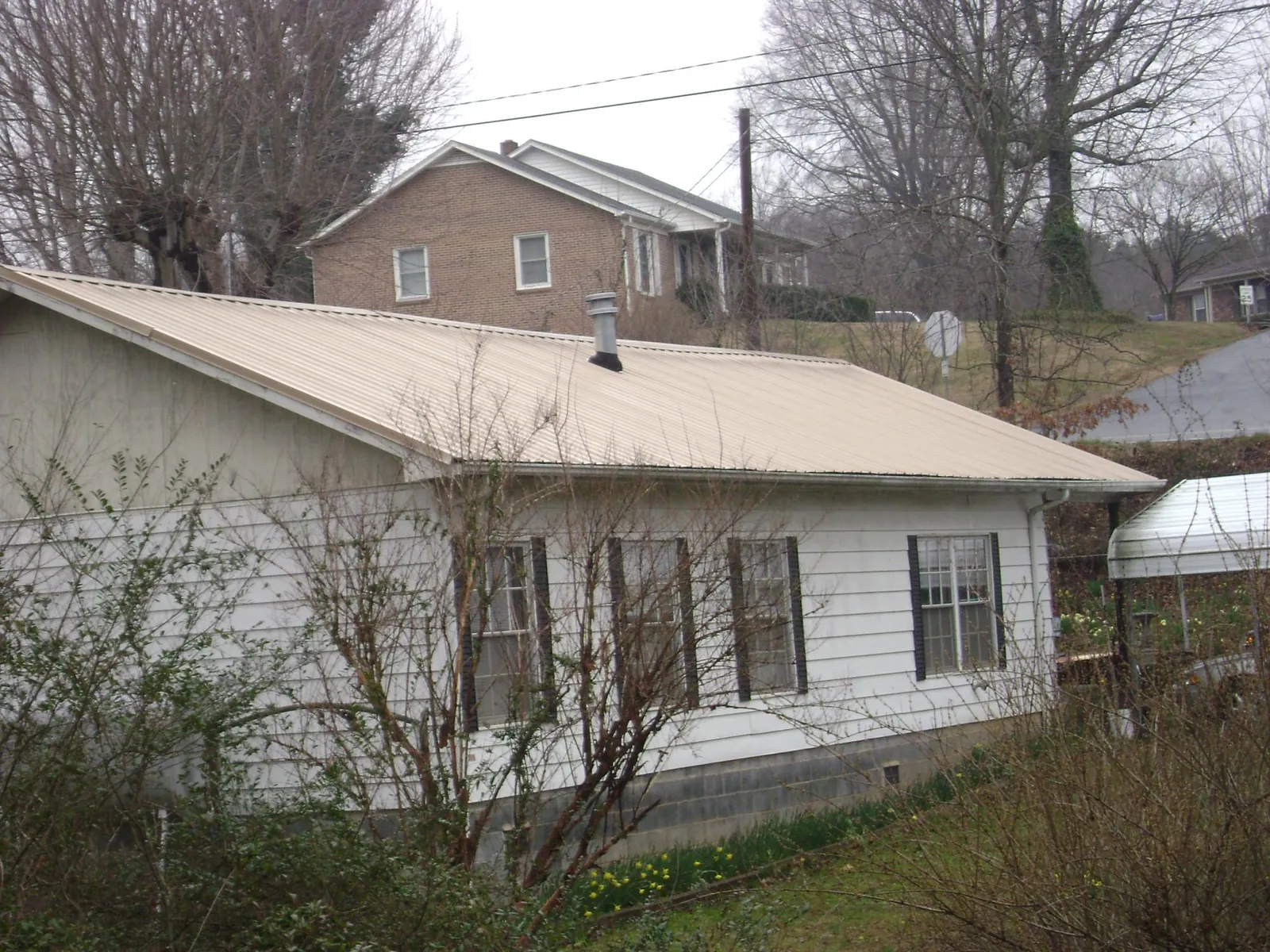 Tan metal roof on a white sided house set into a hillside — Commercial Roofing by Roofing Brothers in Sewell